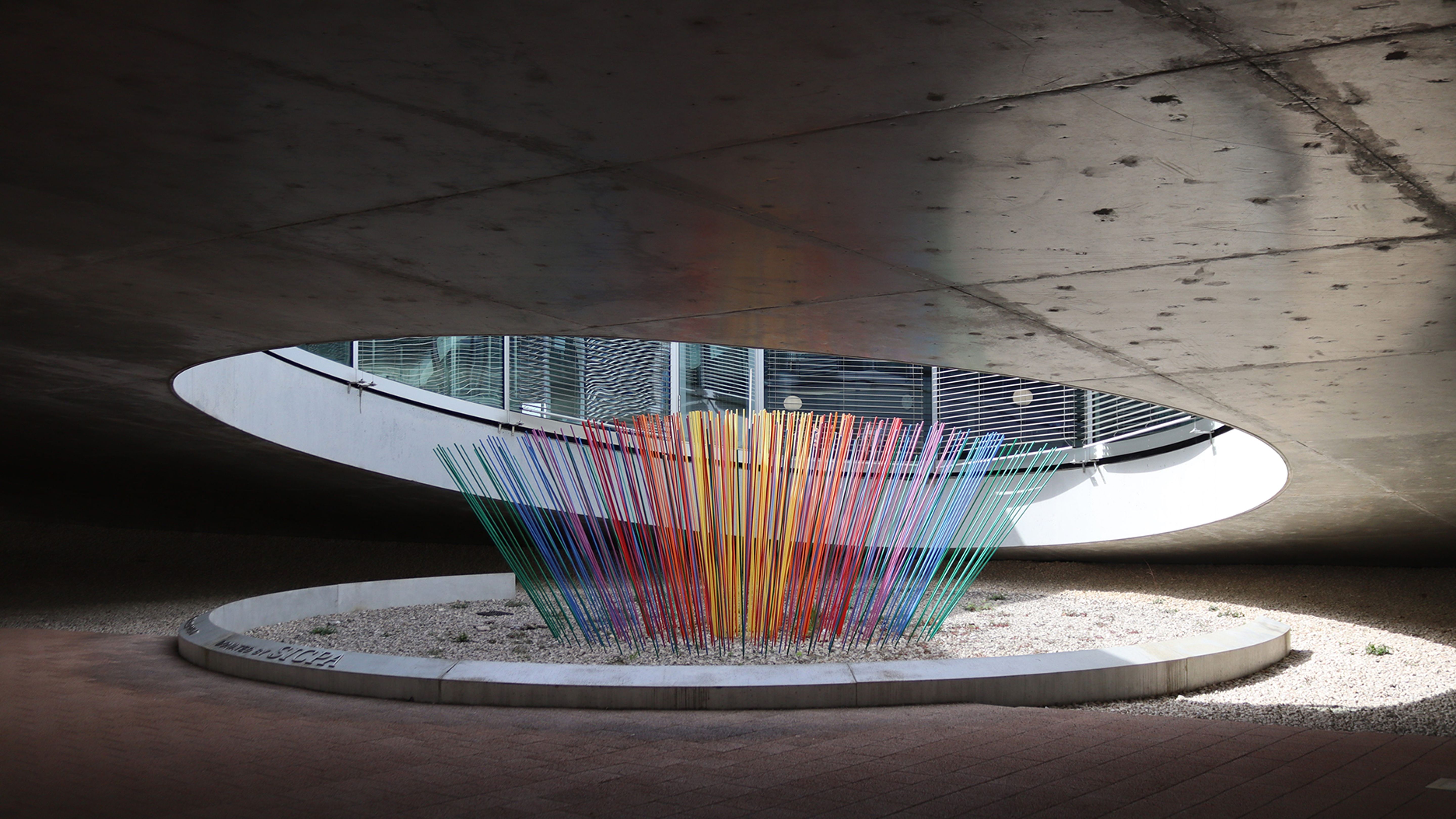 Un’opera d’arte colorata realizzata con bastoni sottili è stata realizzata sotto un tetto in cemento.