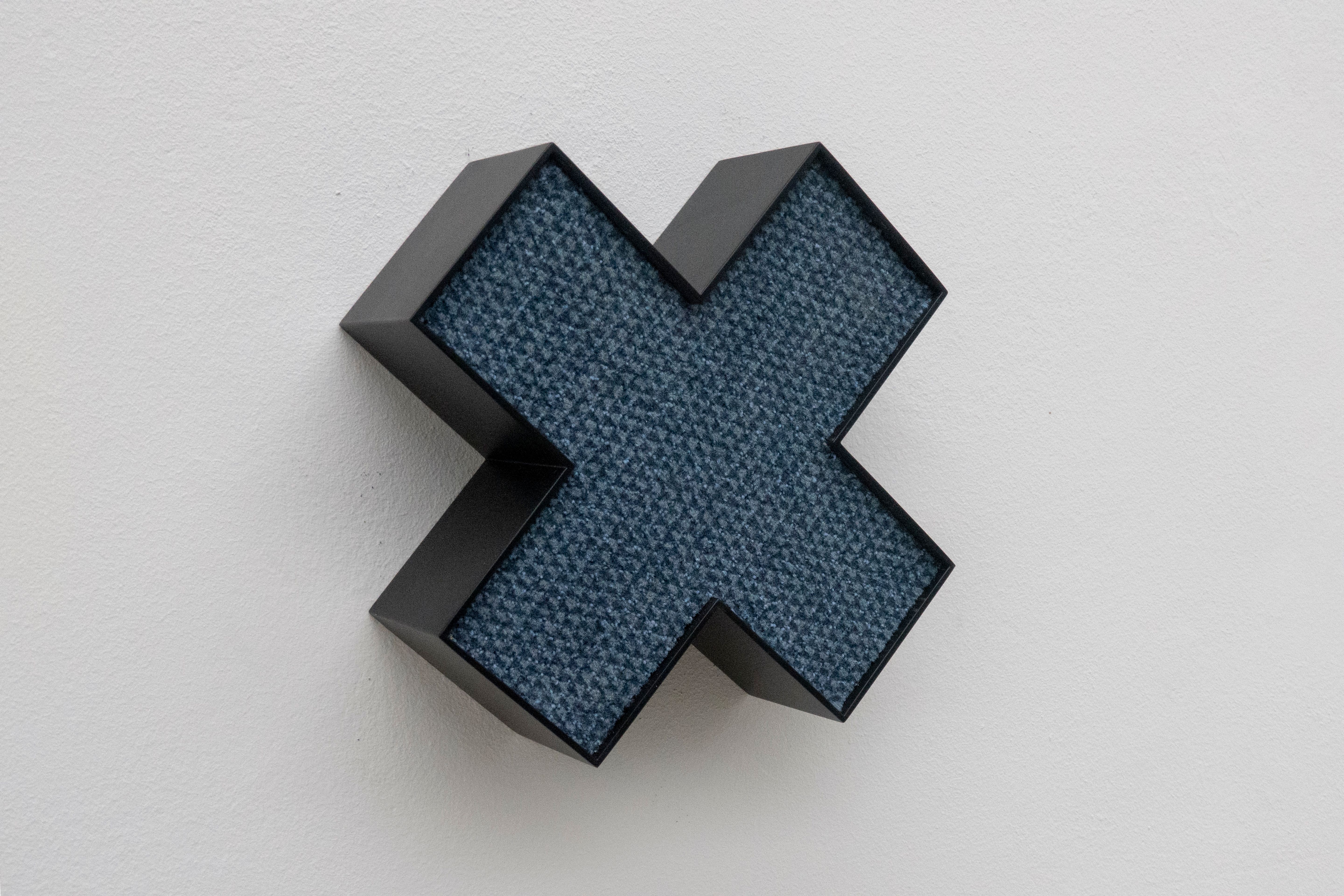 Objet en forme de X avec intérieur bleu sur un mur blanc.