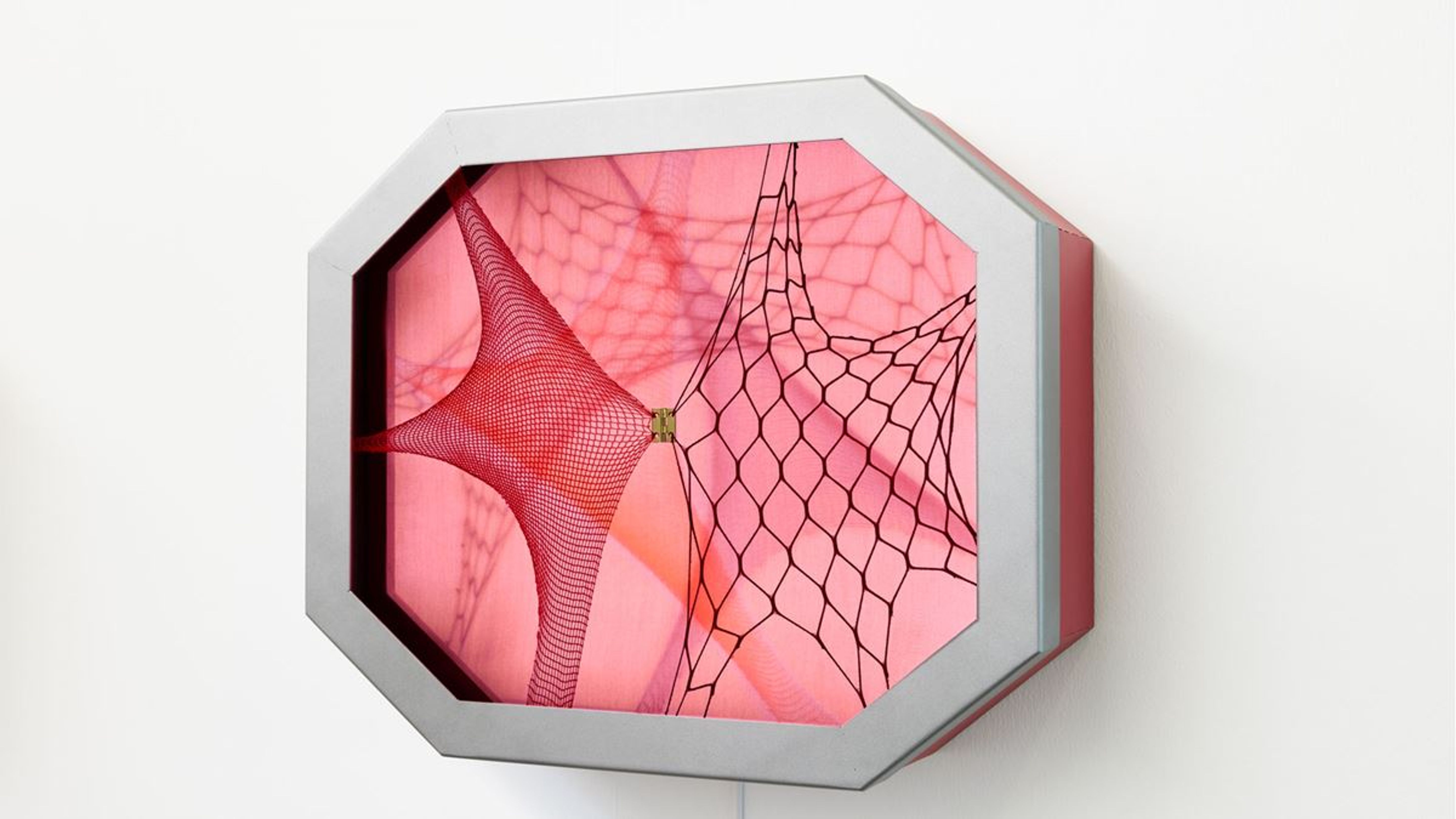 Un objet d’art octogonal avec un fond rose et une toile de filet structurée.