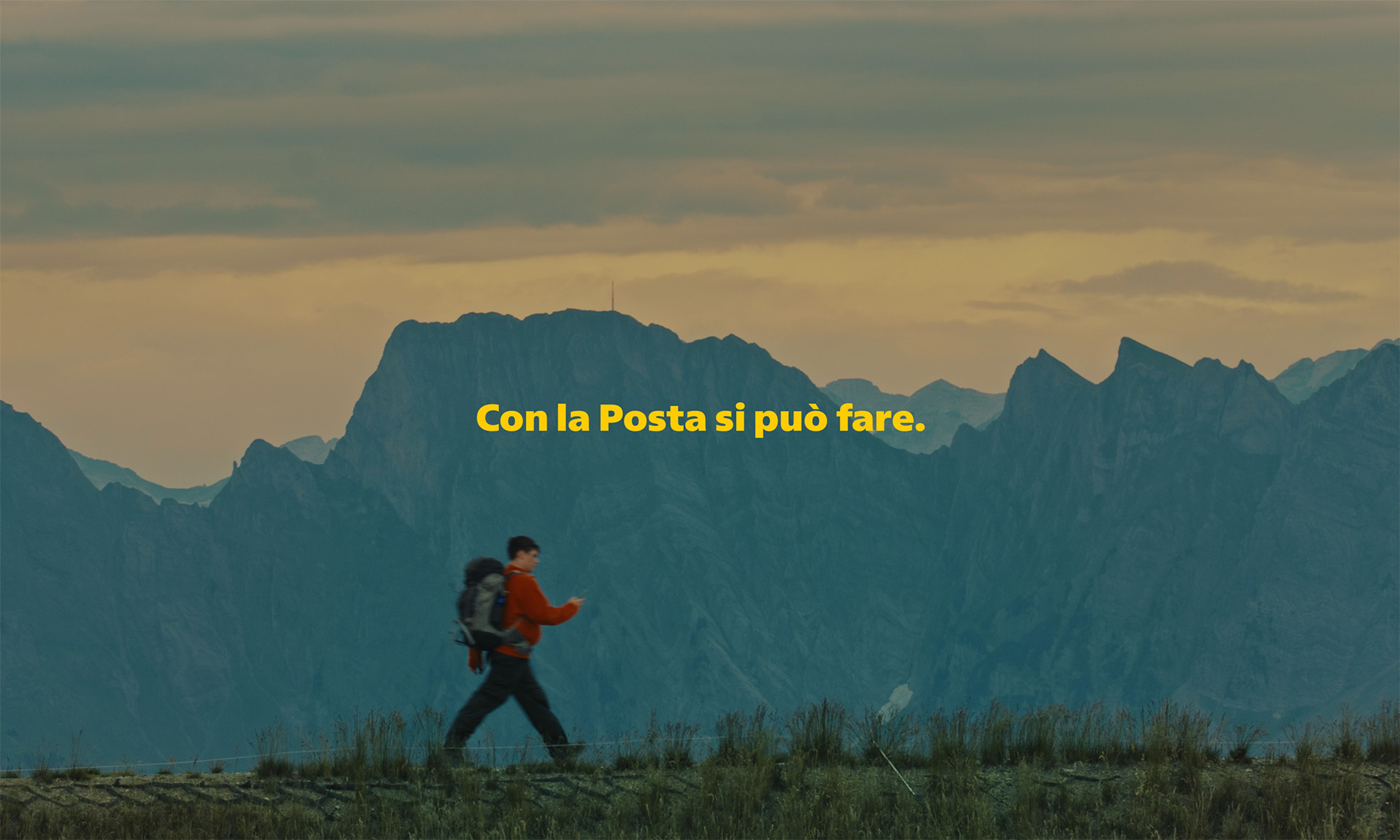 Una persona si trova davanti a un veicolo di trasporto aperto e tiene sollevato uno smartphone che mostra un’interfaccia gialla con diverse icone. Davanti alla persona ci sono scatole e superfici in legno. Sullo sfondo sono visibili alberi, un edificio e una struttura coperta. Al centro dell’immagine compare il testo giallo: “Con la Posta si puo fare”