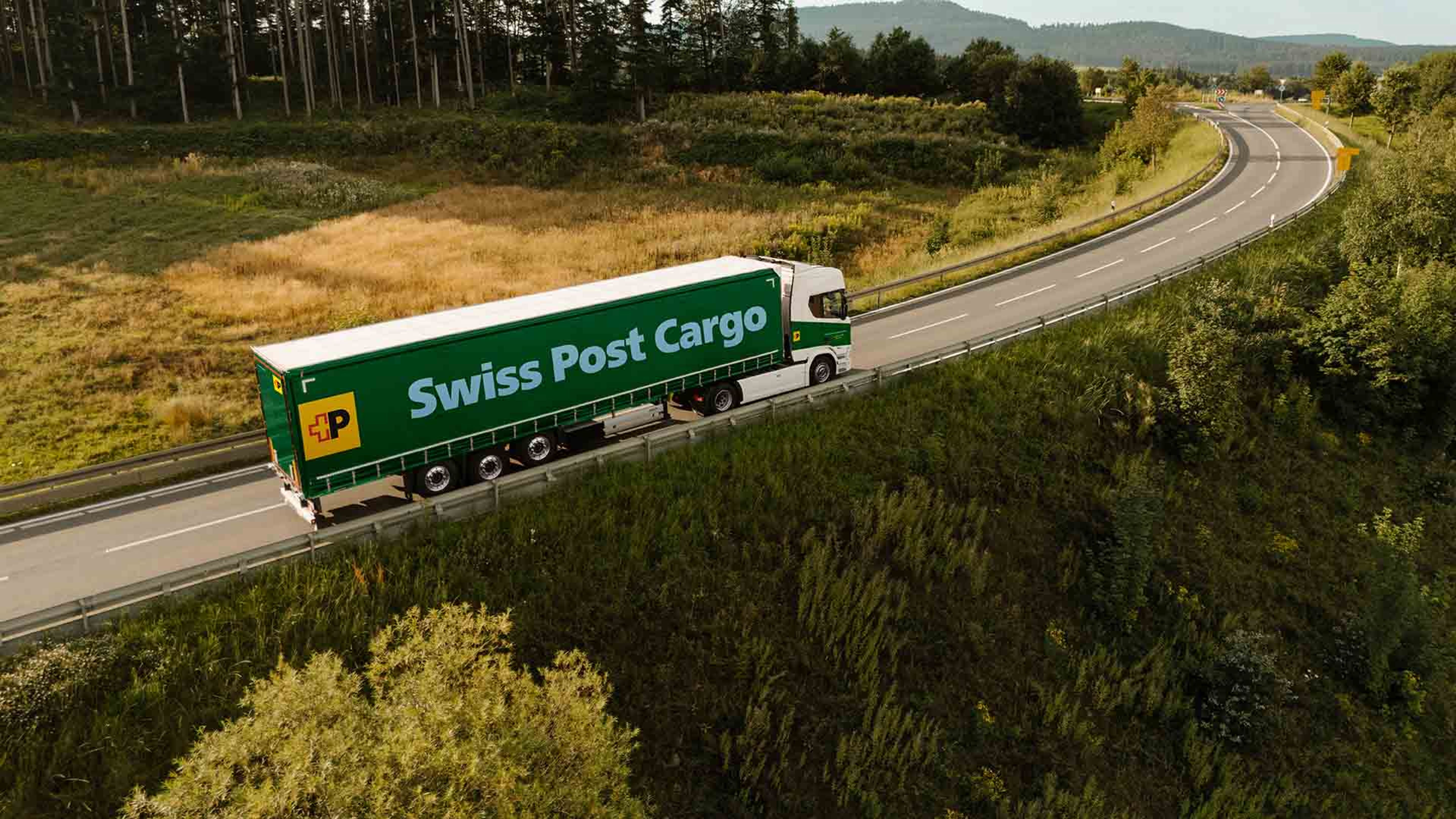 Ein LKW von Swiss Post Cargo fährt auf einer Landstrasse und transportiert Waren.