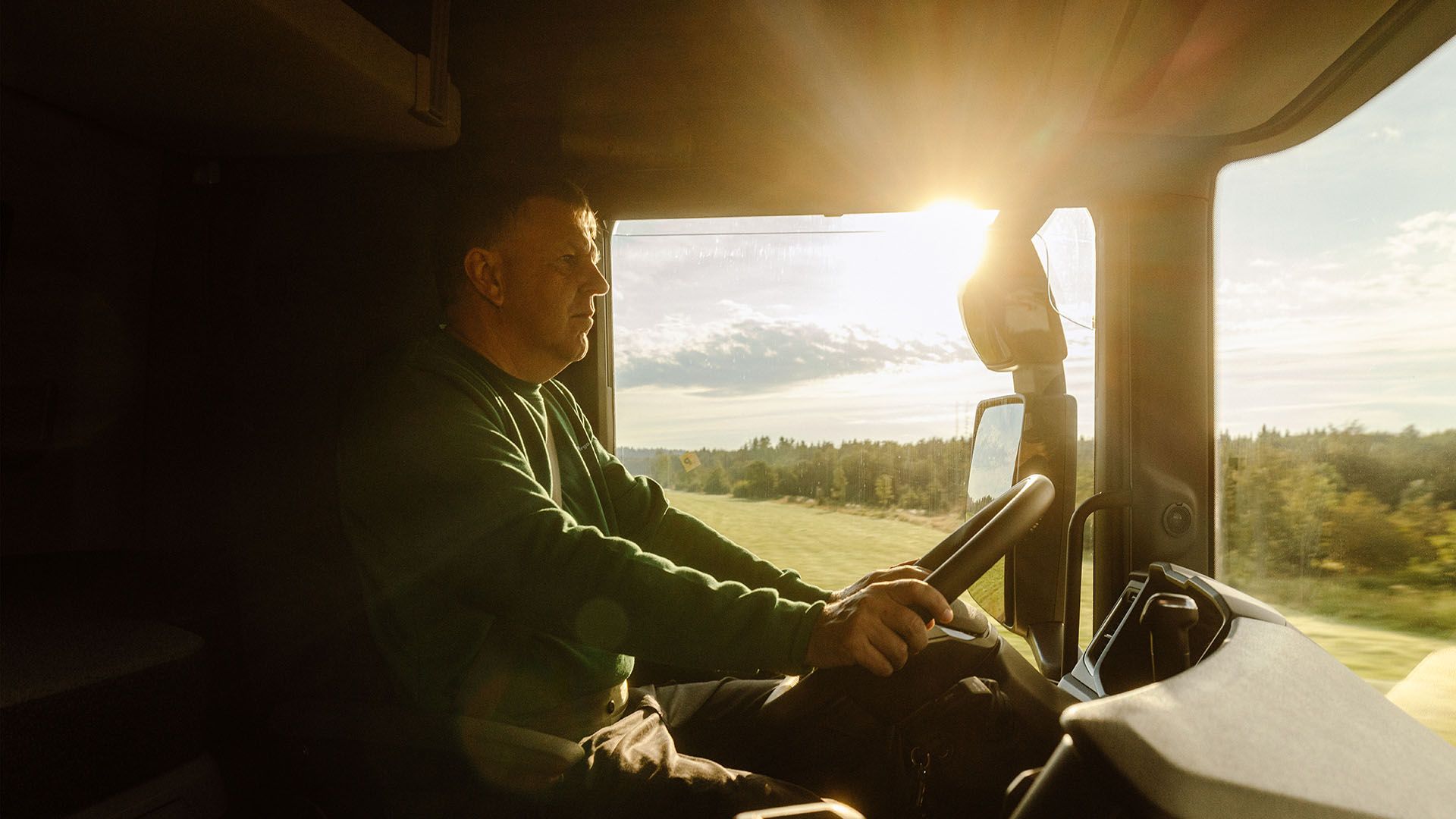 Ein LKW-Fahrer von Swiss Post Cargo steuert sein Fahrzeug auf einer Direktfahrt durch eine sonnige Landschaft.