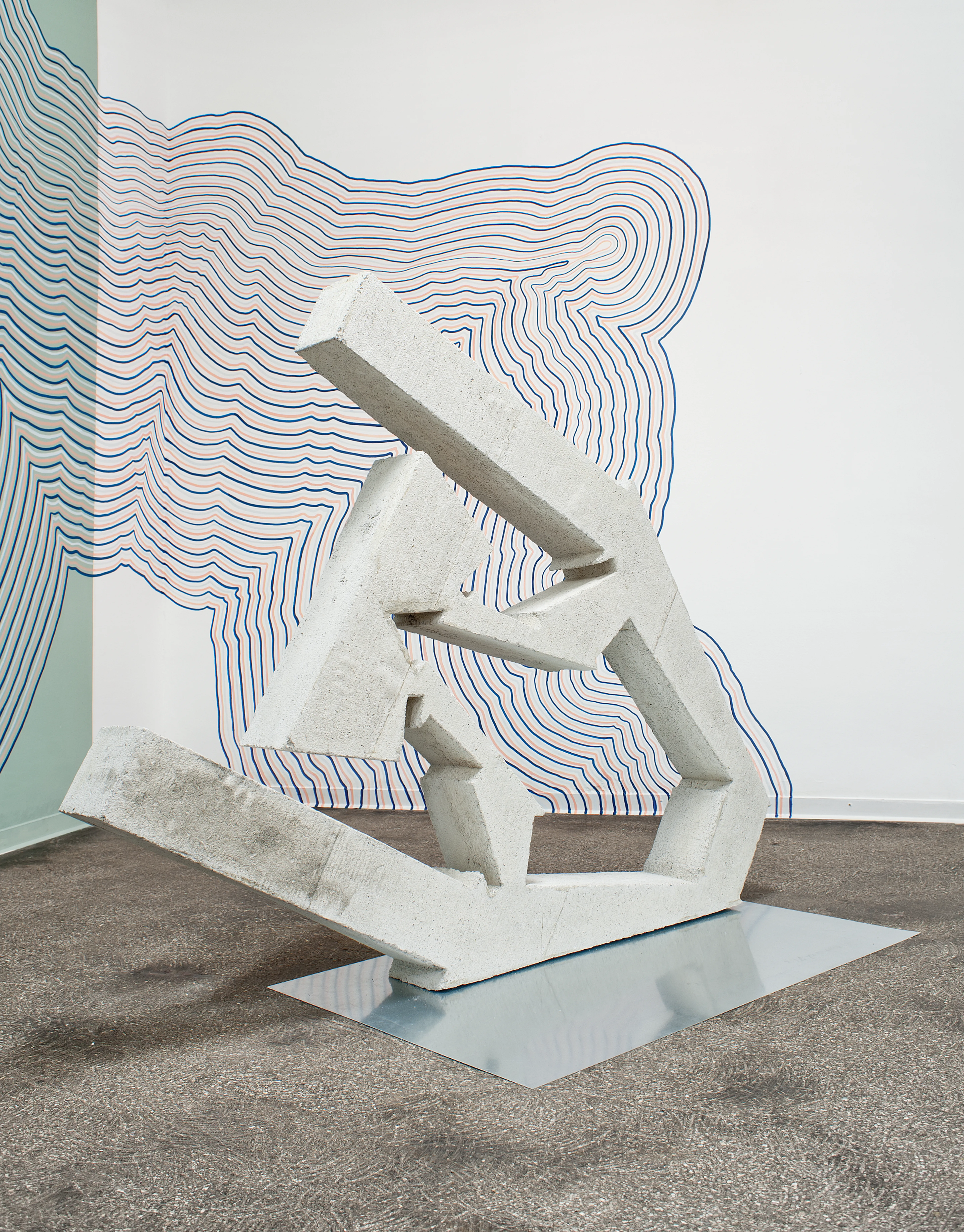 Une sculpture en pierre abstraite devant un mur à motifs.