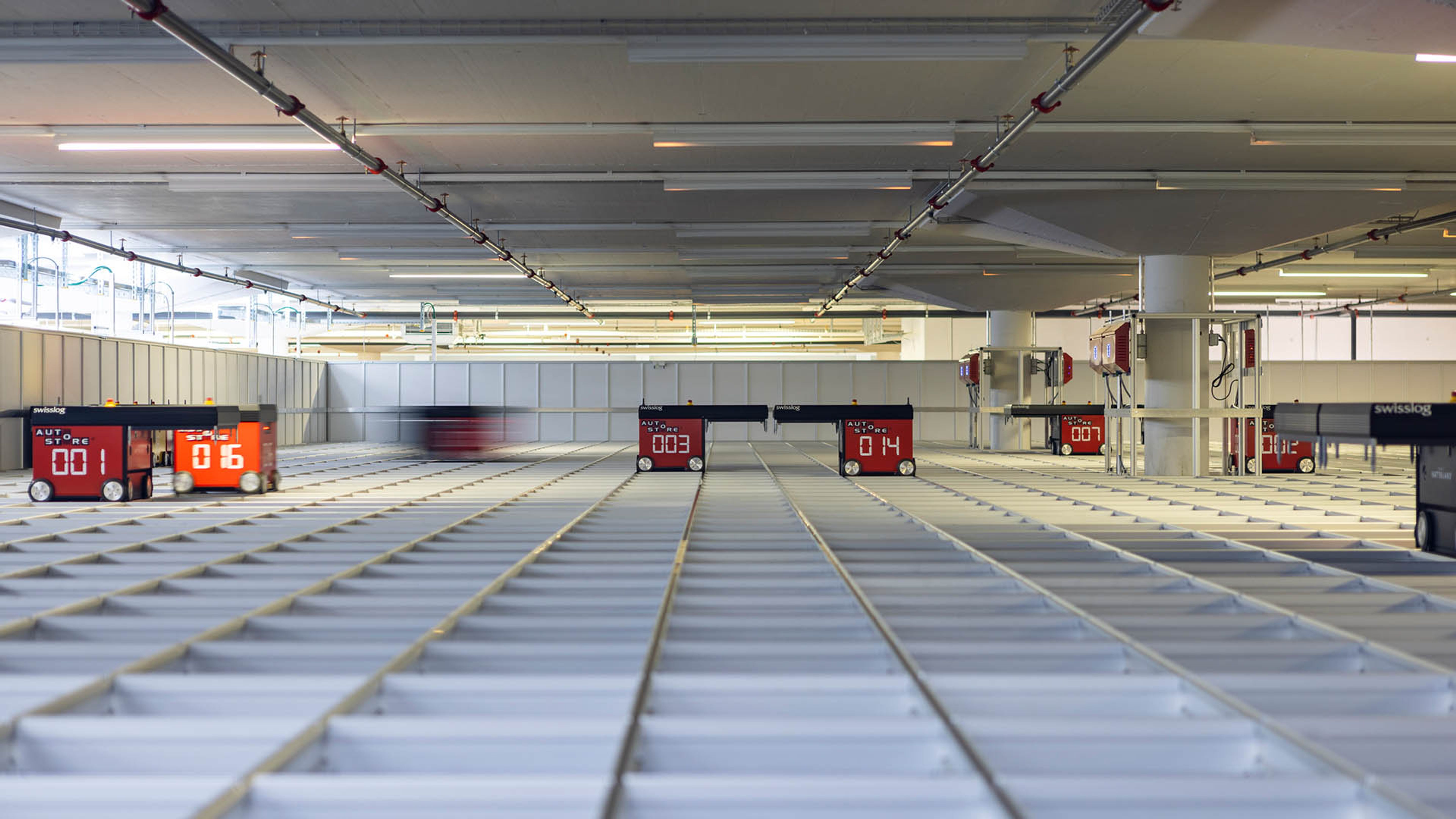 Sistema di stoccaggio automatizzato con robot autonomi che si muovono su una griglia di contenitori. I robot Swisslog si spostano con precisione sui binari per immagazzinare e prelevare la merce in modo efficiente.