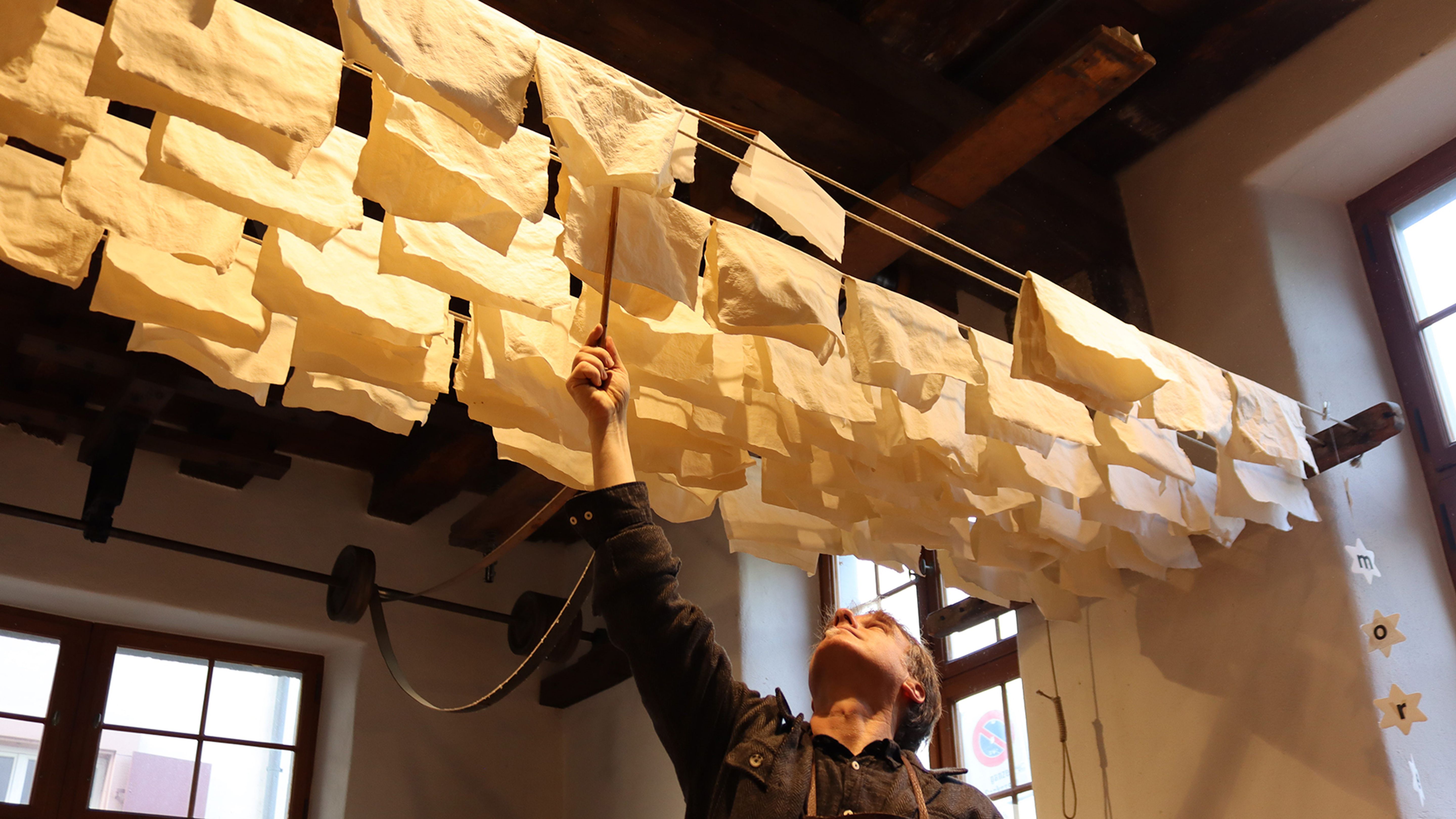 Una persona ispeziona i pezzi di carta gialli sospesi in un locale illuminato termicamente con una copertura in legno.