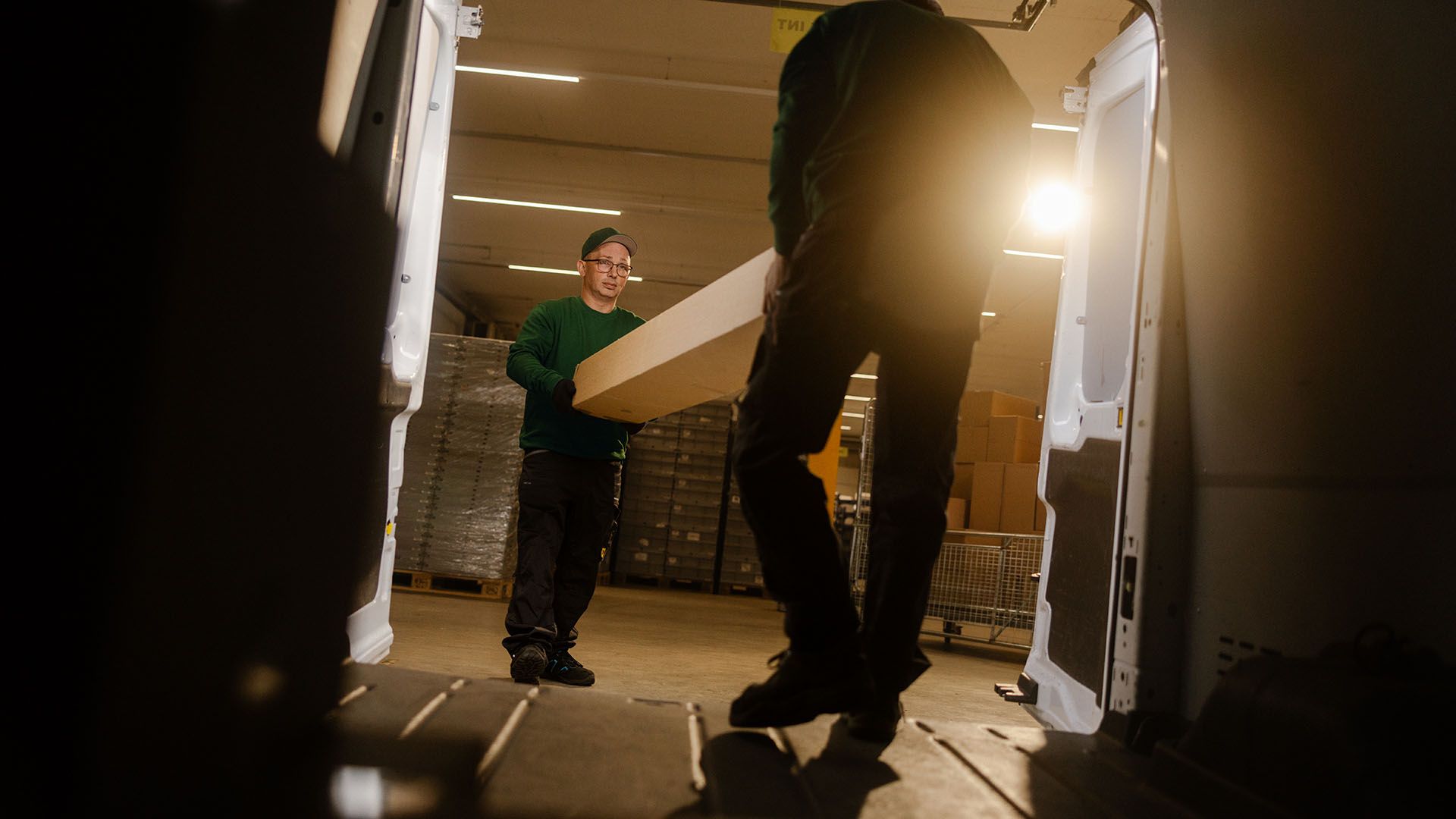 Two Swiss Post Cargo employees load spare parts into a service vehicle at night.