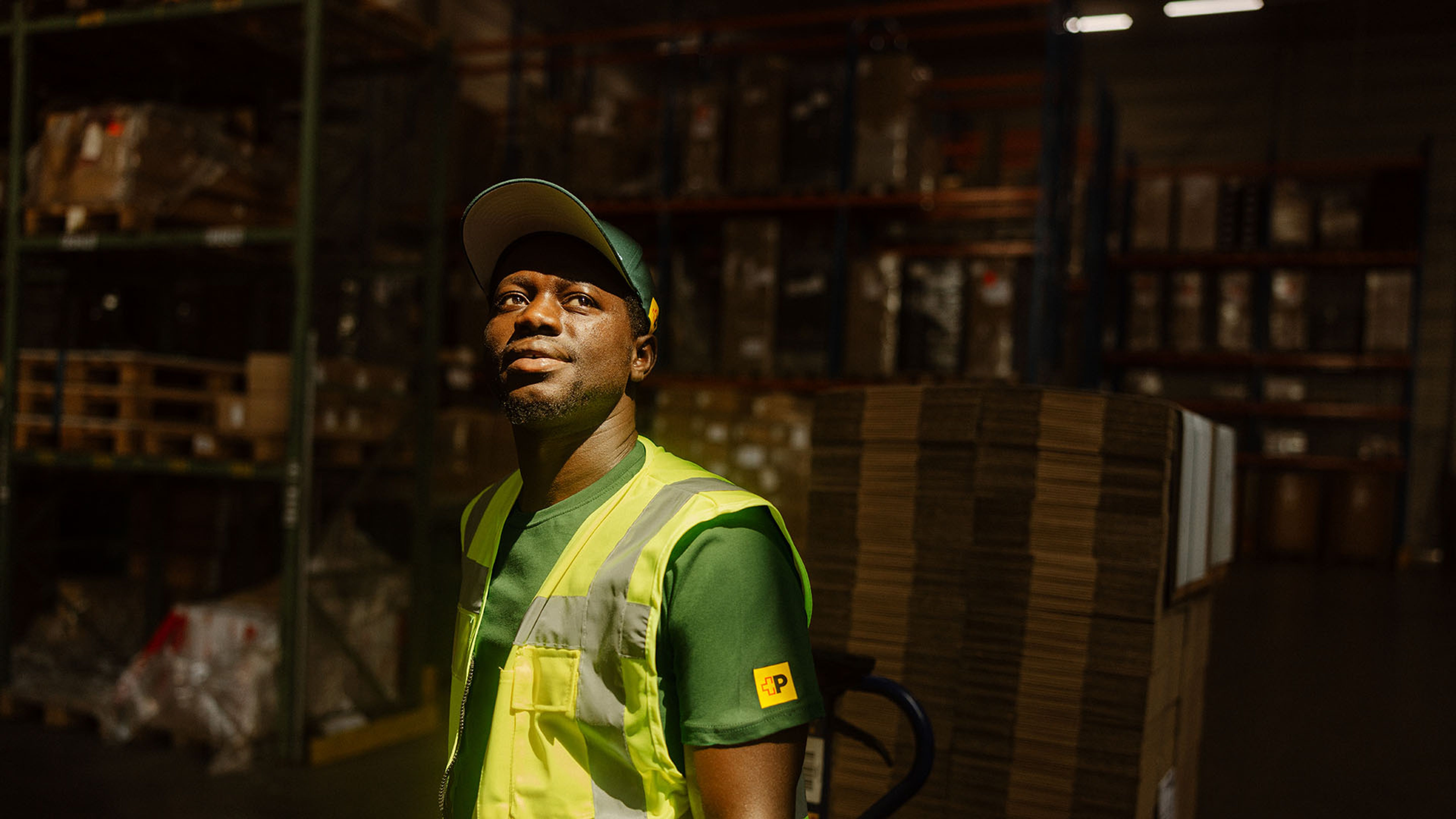 Le collaborateur Swiss Post Cargo avec veste réfléchissante se tient devant le local de stockage contenant les colis.