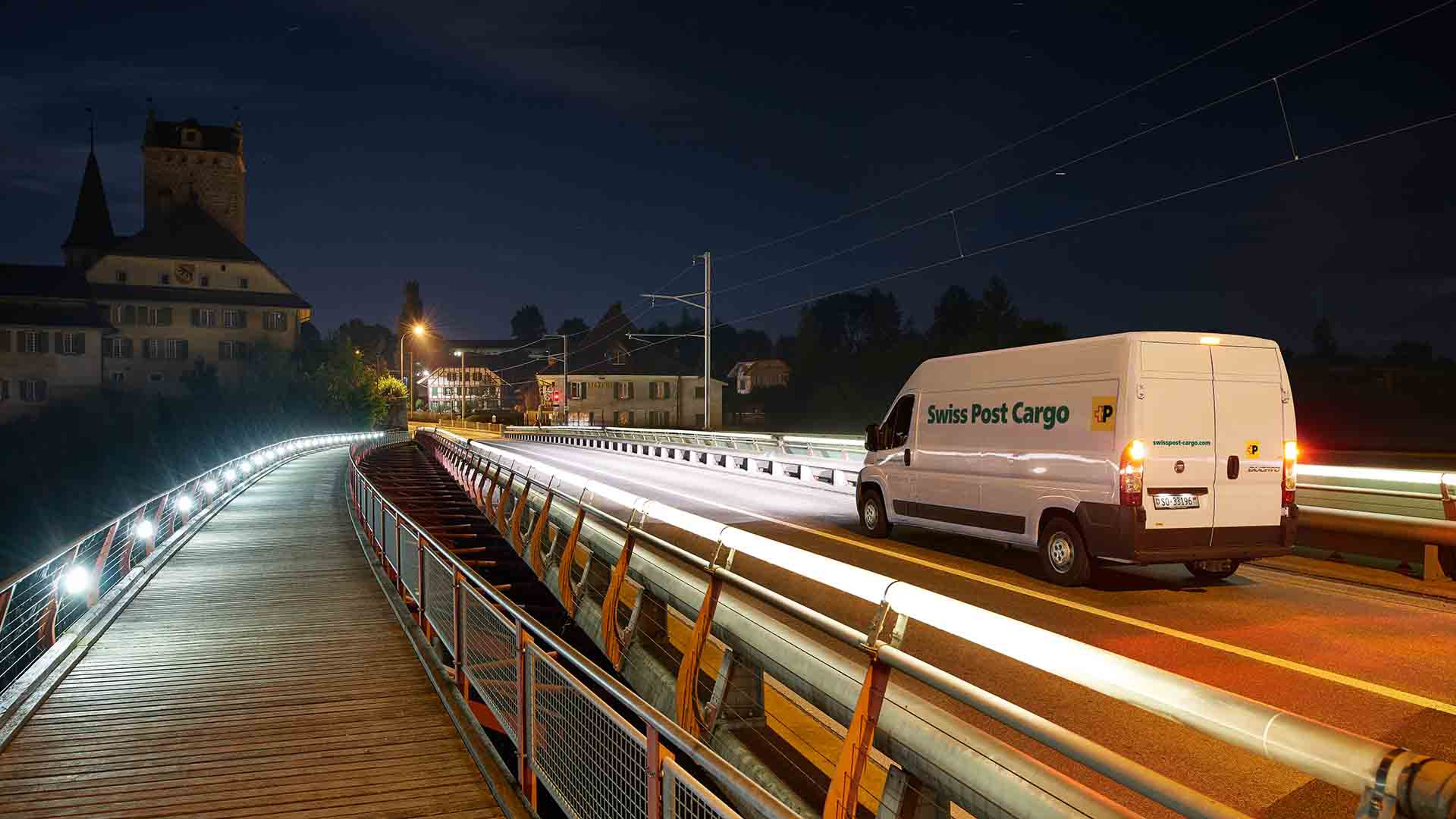 Un veicolo di consegna di Swiss Post Cargo attraversa un ponte di notte con una consegna express.