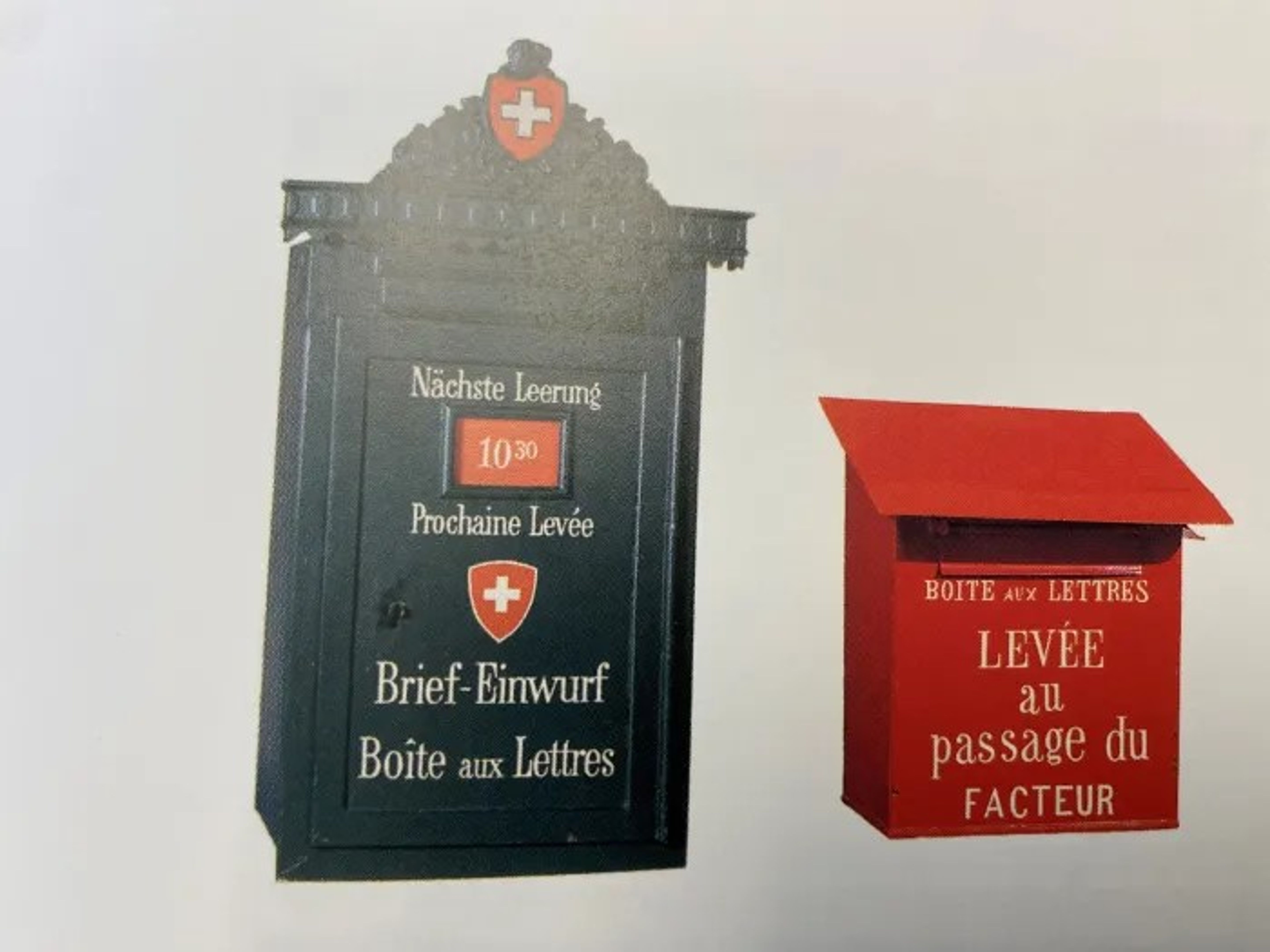 Due cassette postali storiche: a sinistra una cassetta nera con stemma svizzero, ornamento decorativo e scritta « Brief-Einwurf / Boîte aux Lettres » e « Nächste Leerung 10:30 ». A destra una cassetta rossa con la scritta « Boîte aux Lettres – Levée au passage du facteur ».