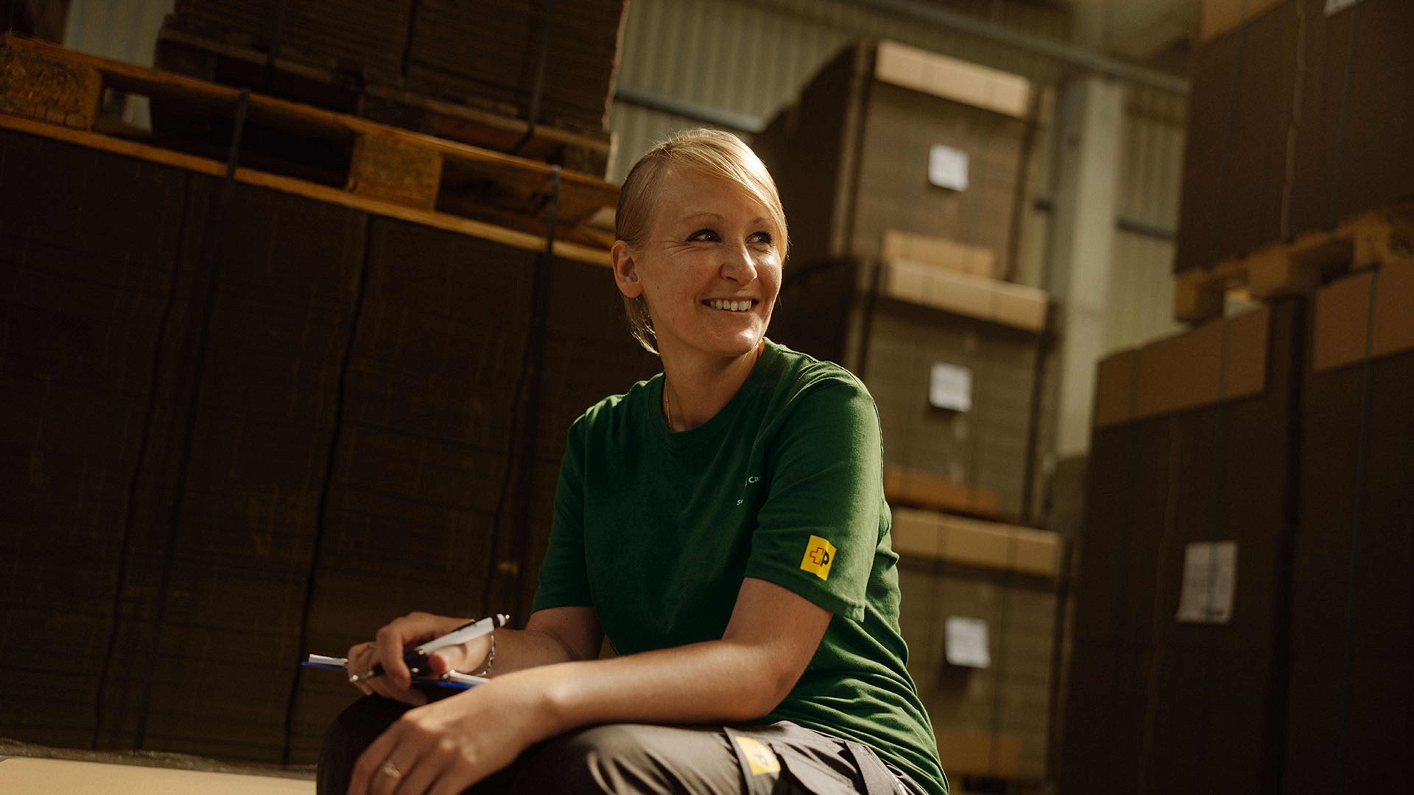 Une collaboratrice Swiss Post Cargo souriante devant un rayon dans le local de stockage.
