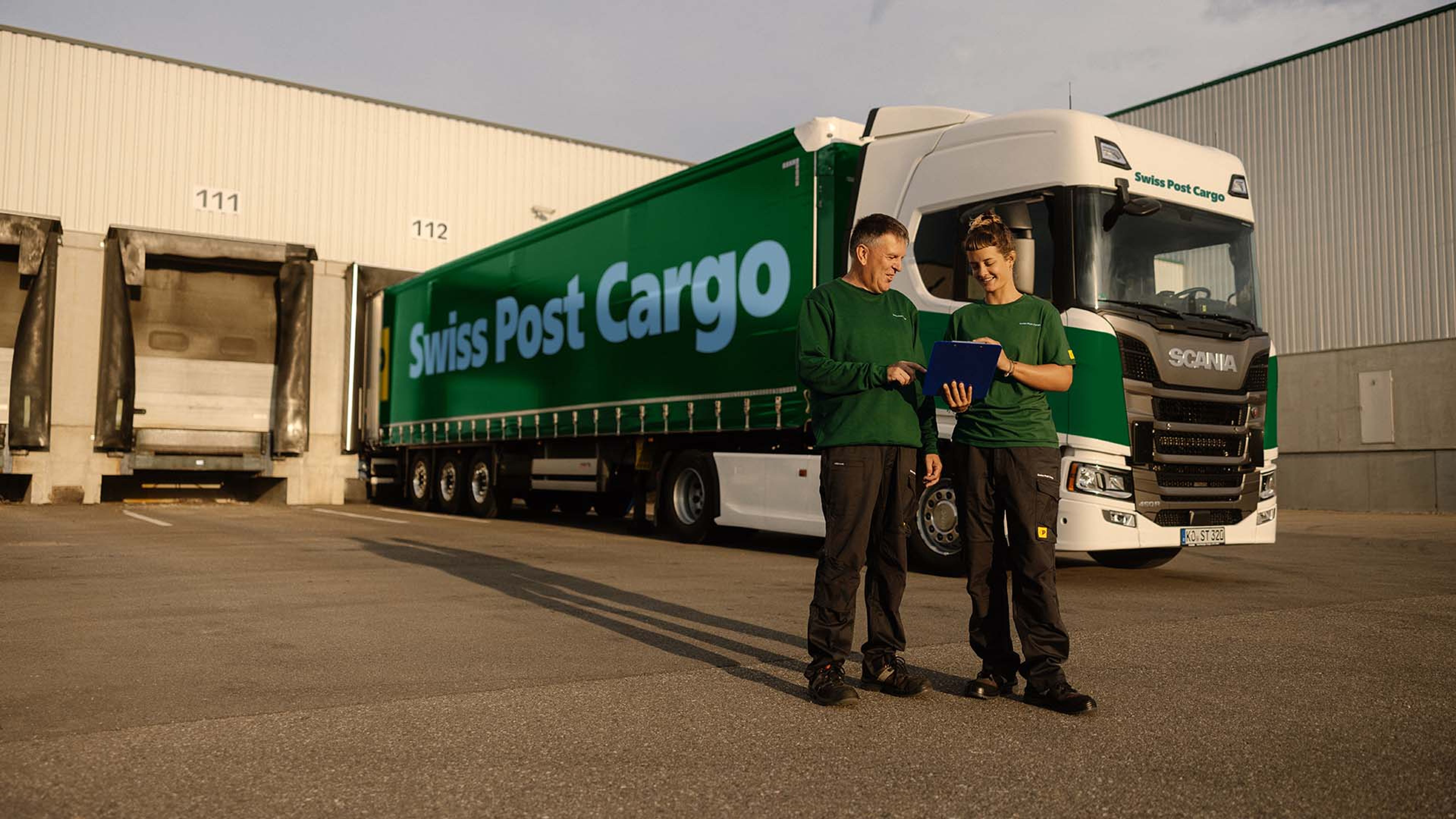 Zwei Swiss Post Cargo Mitarbeiter stehen vor einem Swiss Post Cargo LKW.