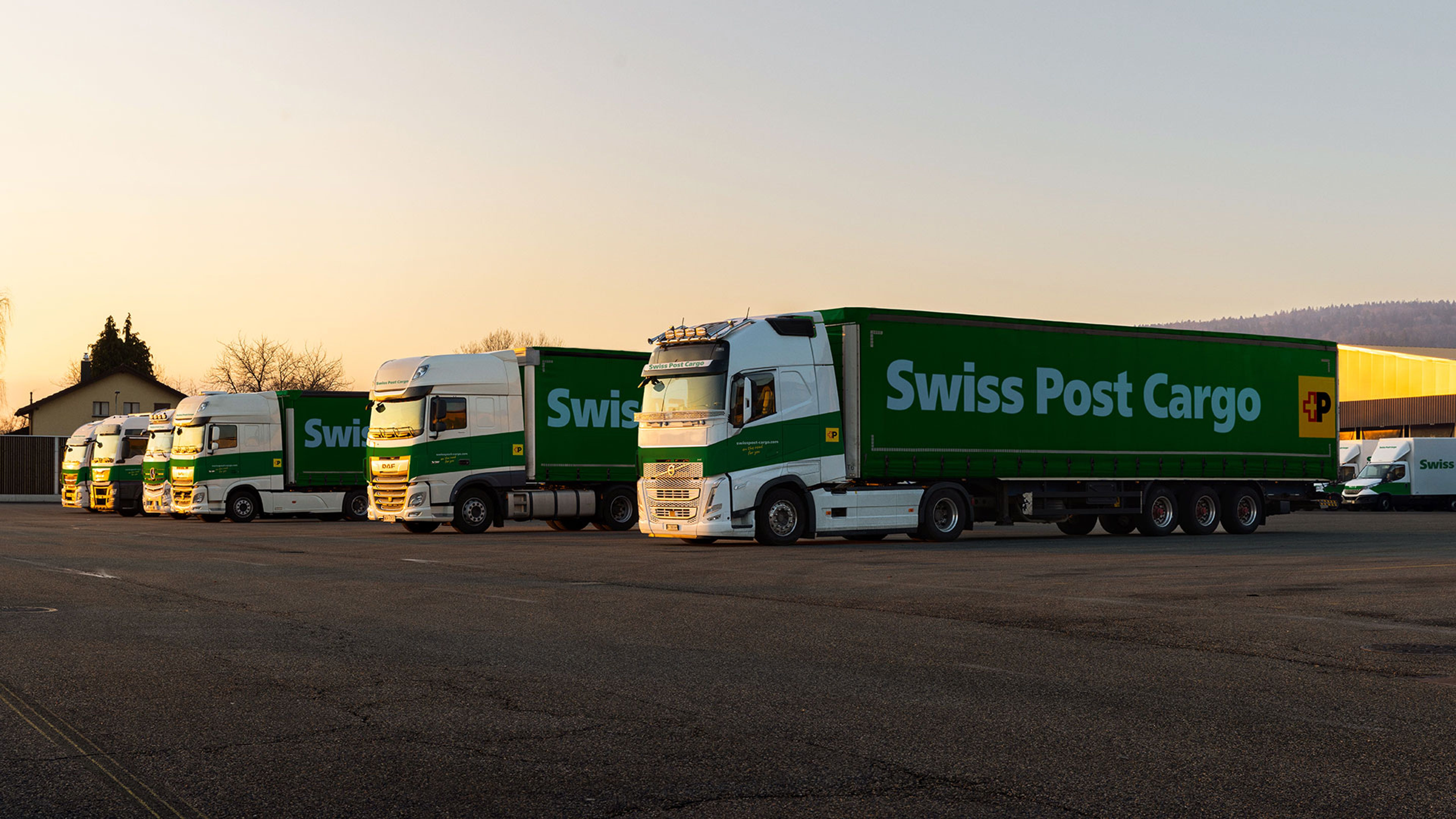 Al tramonto gli autocarri Swiss Post Cargo si trovano davanti al centro logistico.