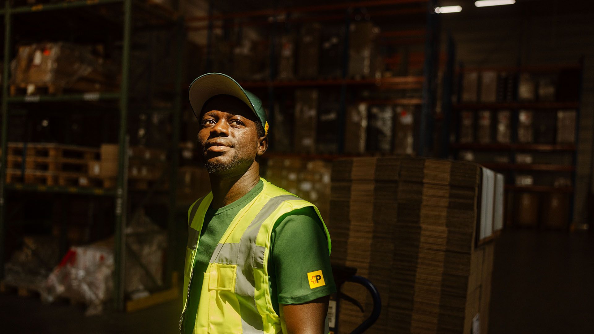 Swiss Post Cargo employee in high visibility vest stands in front of storage room with parcels.