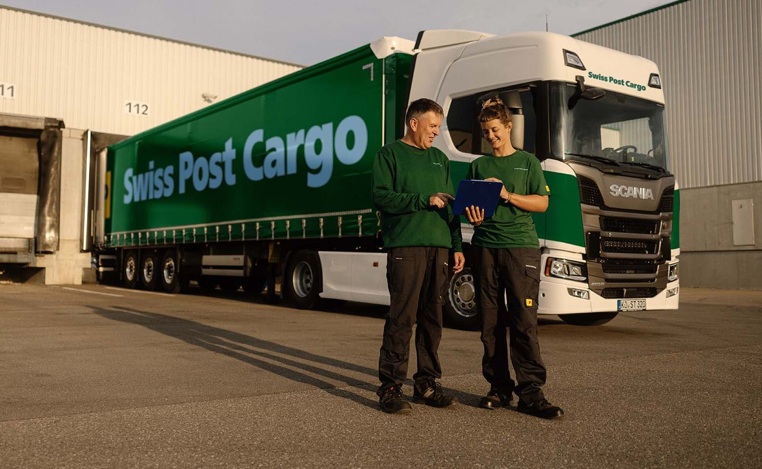 Two Swiss Post Cargo employees stand in front of a Swiss Post Cargo lorry.
