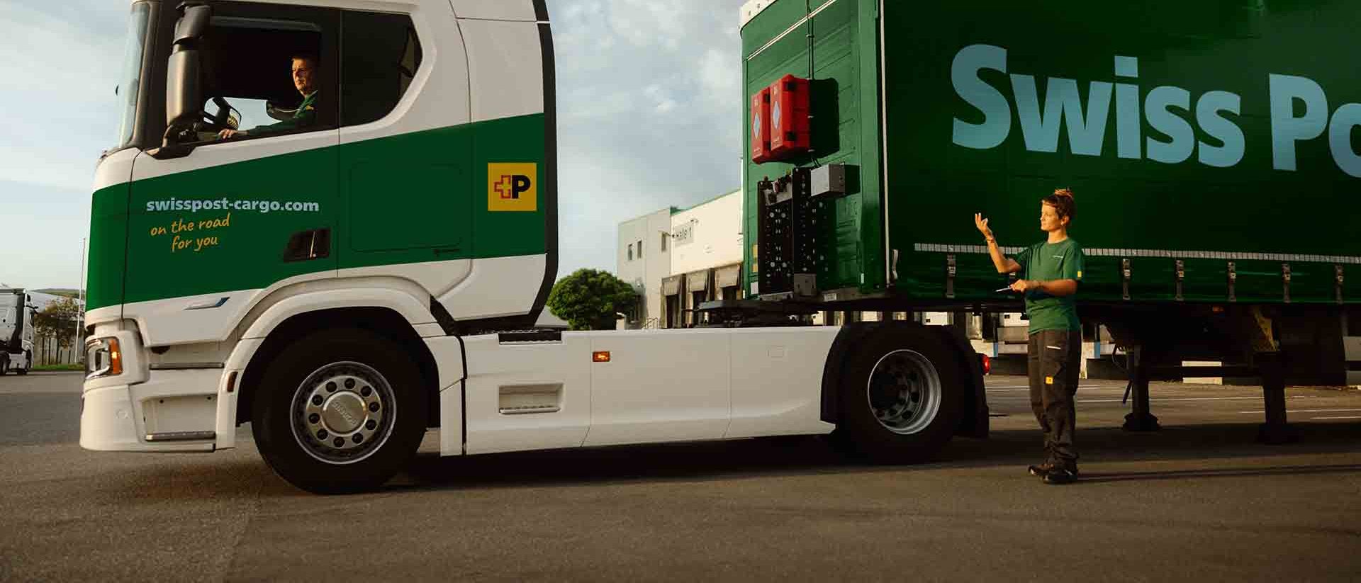 Ein Swiss Post Cargo LKW-Fahrer kuppelt mit der Hilfe einer Kollegin einen Anhänger an.