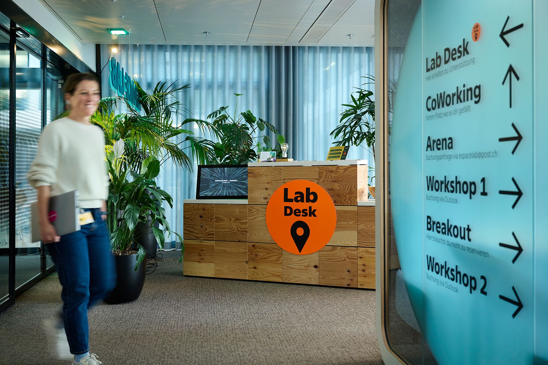 A person walks past a reception desk with a “Lab Desk” sign in a modern office.
