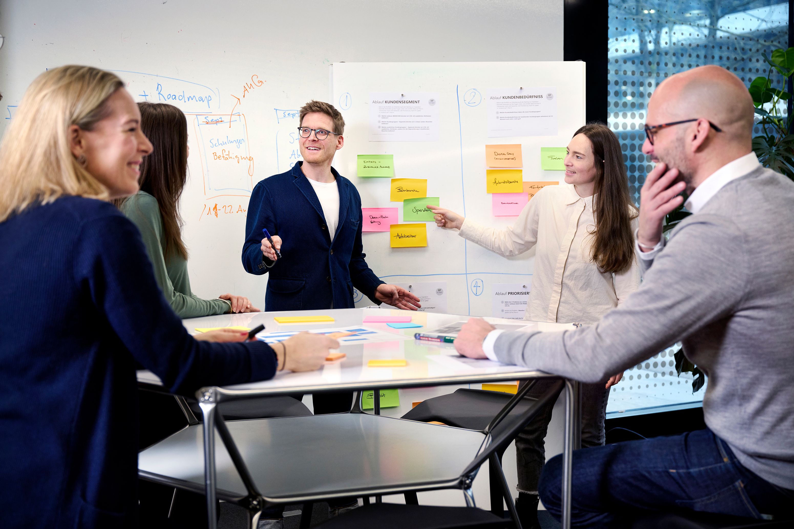 A group of people in an office discussing in front of a whiteboard covered with notes.