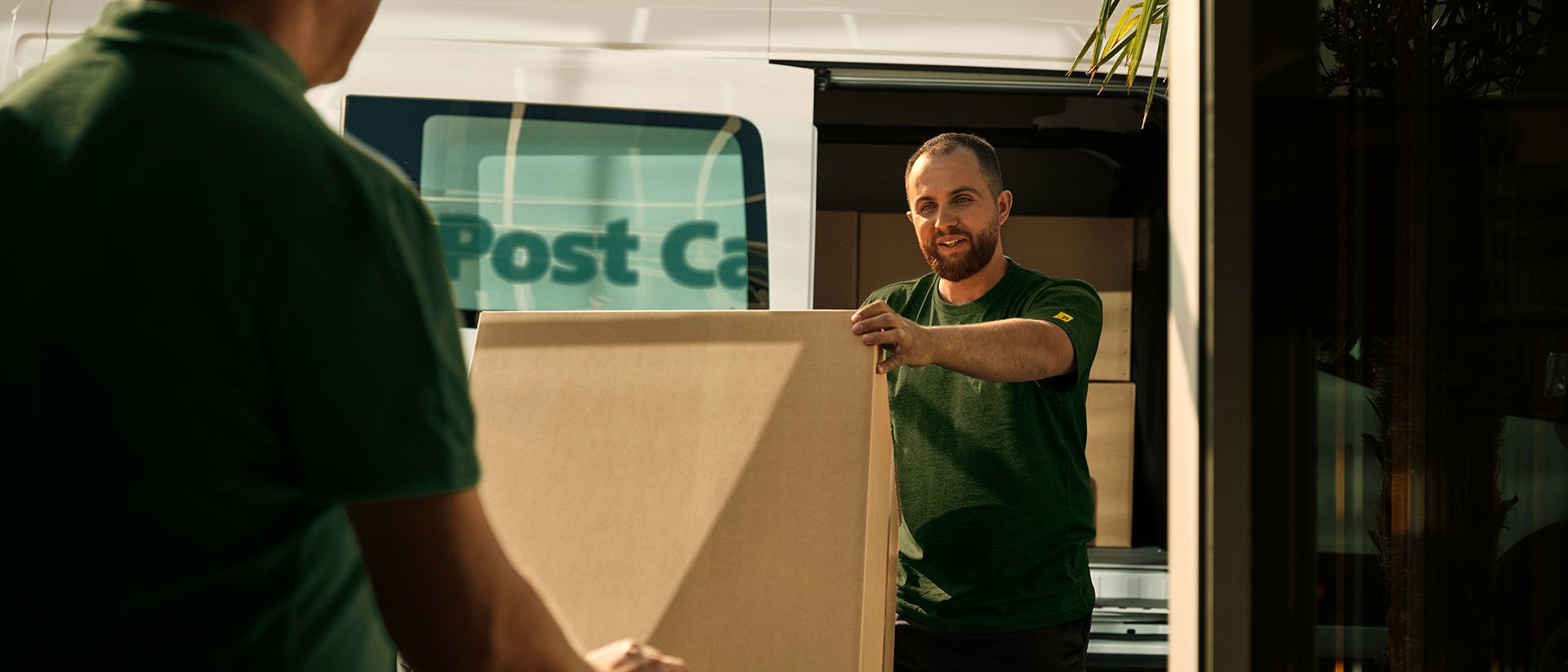 Zwei Swiss Post Cargo Mitarbeitende laden eine sperrige Lieferung aus einem Fahrzeug aus.