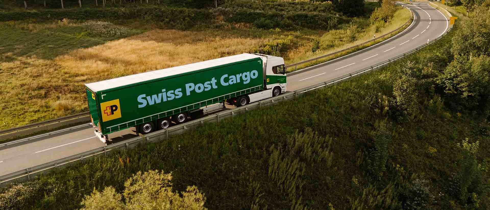 Ein LKW von Swiss Post Cargo fährt auf einer Landstrasse und transportiert Waren.