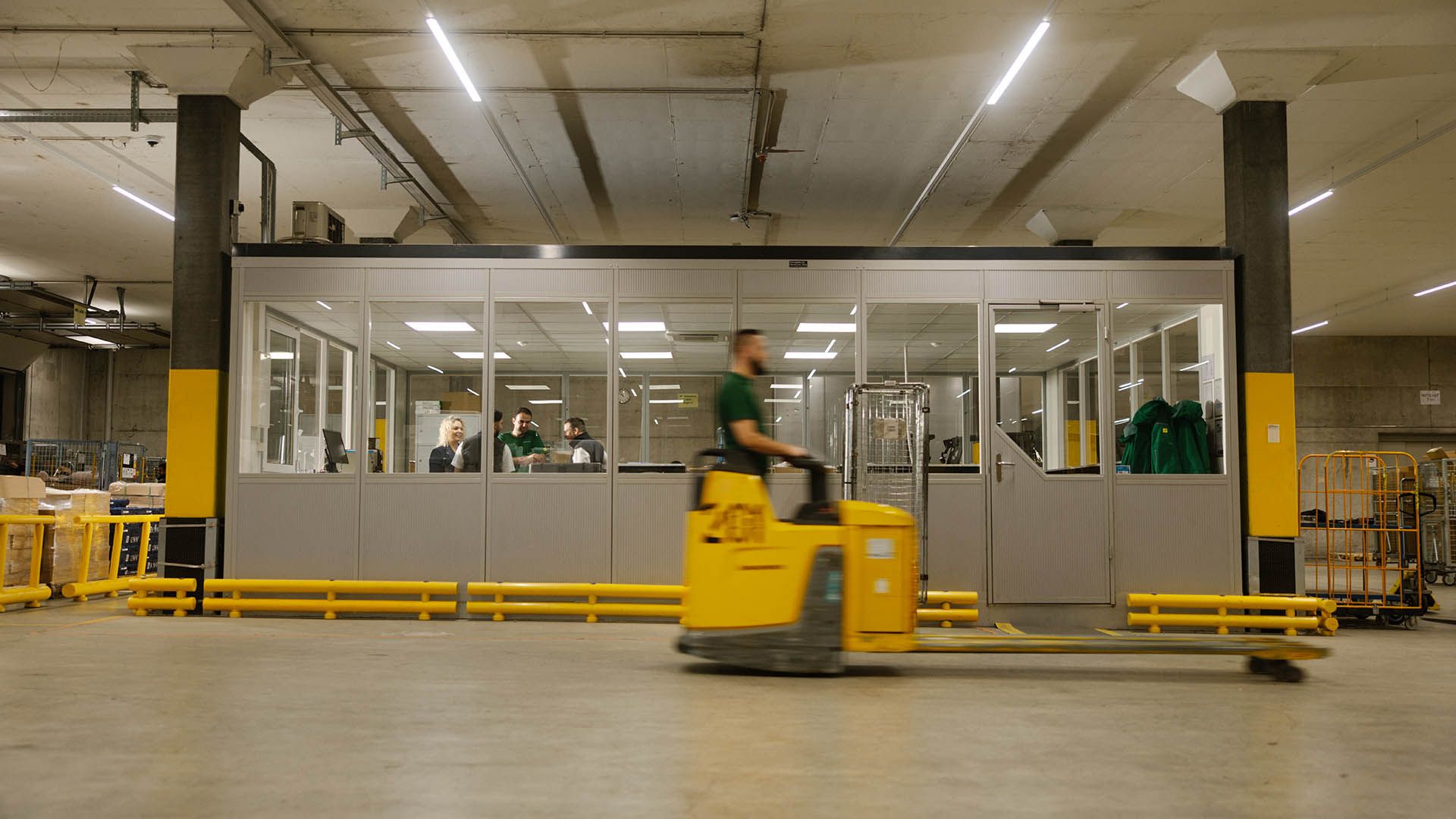 In einer Lagerhalle fährt ein Swiss Post Cargo Mitarbeiter auf einem Hubwagen an einem verglasten Raum vorbei.