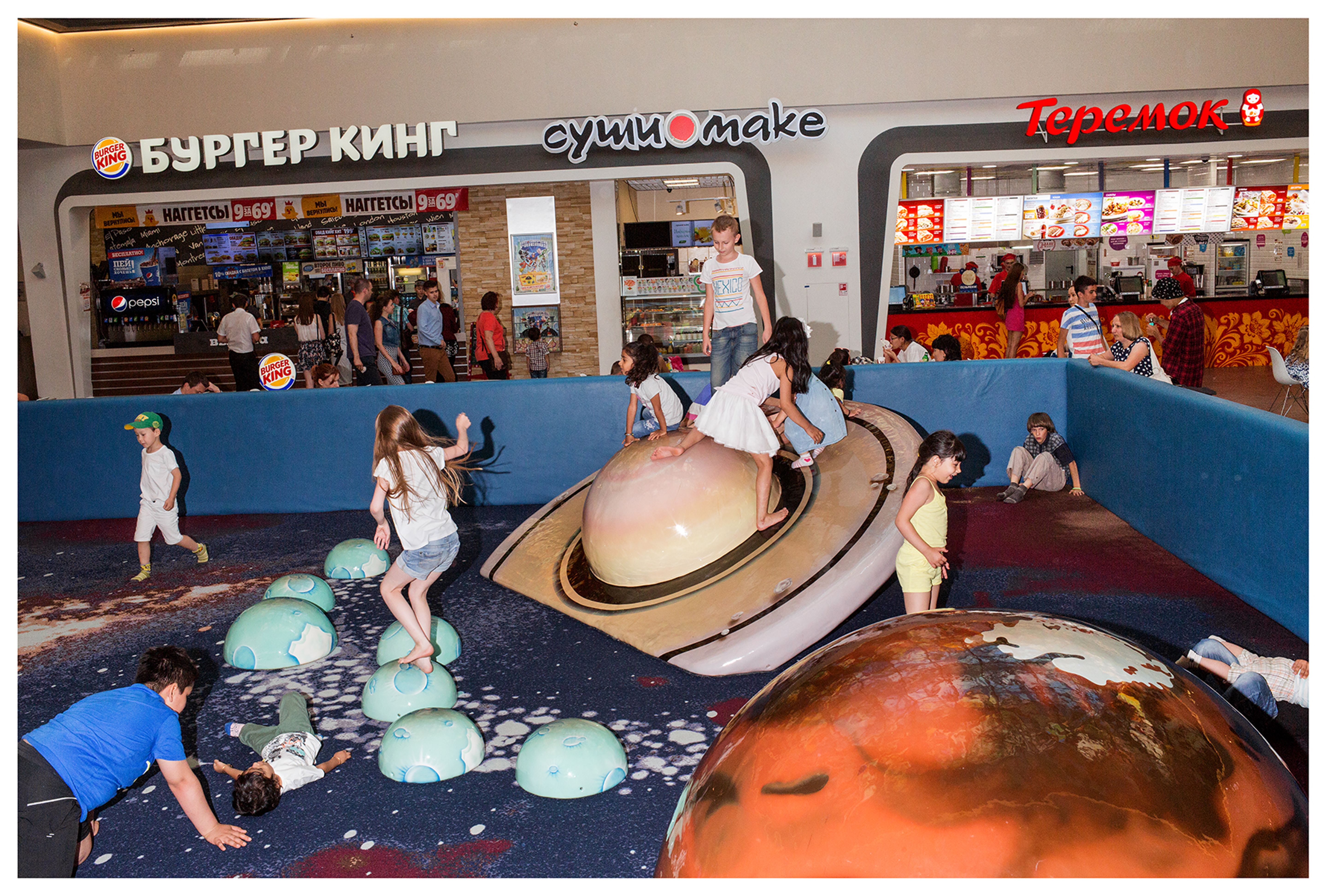 I bambini giocano su strutture a forma di pianeta in un luminoso centro commerciale.