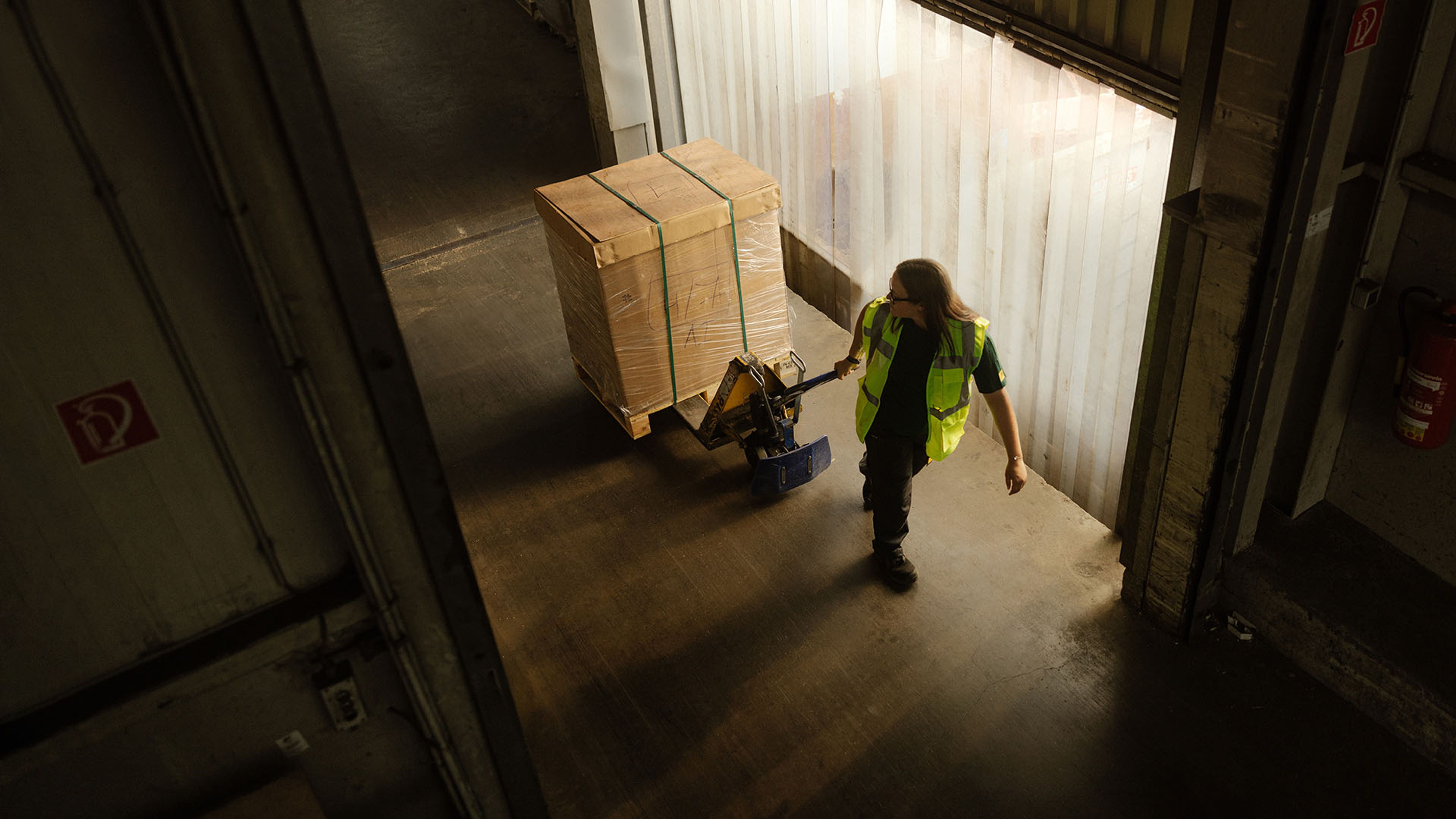 A Swiss Post Cargo warehouse worker moves general cargo on a pallet jack into an elevator.