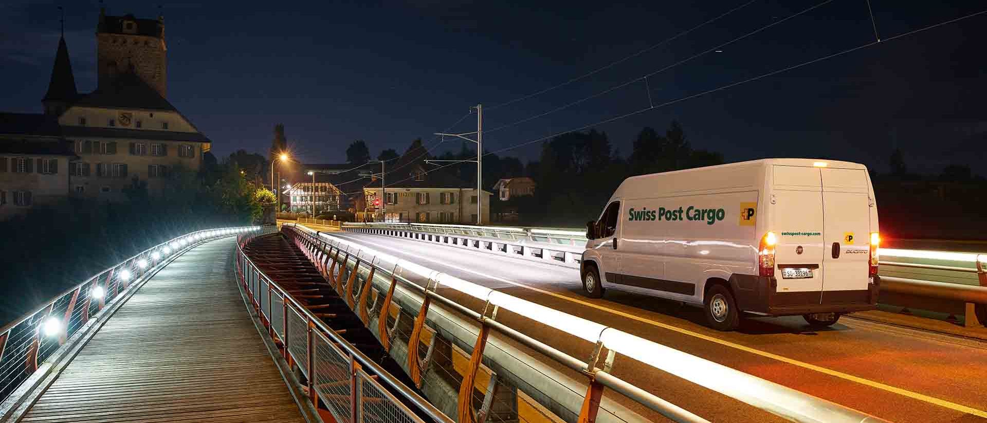 Un veicolo di consegna di Swiss Post Cargo attraversa un ponte di notte con una consegna express.