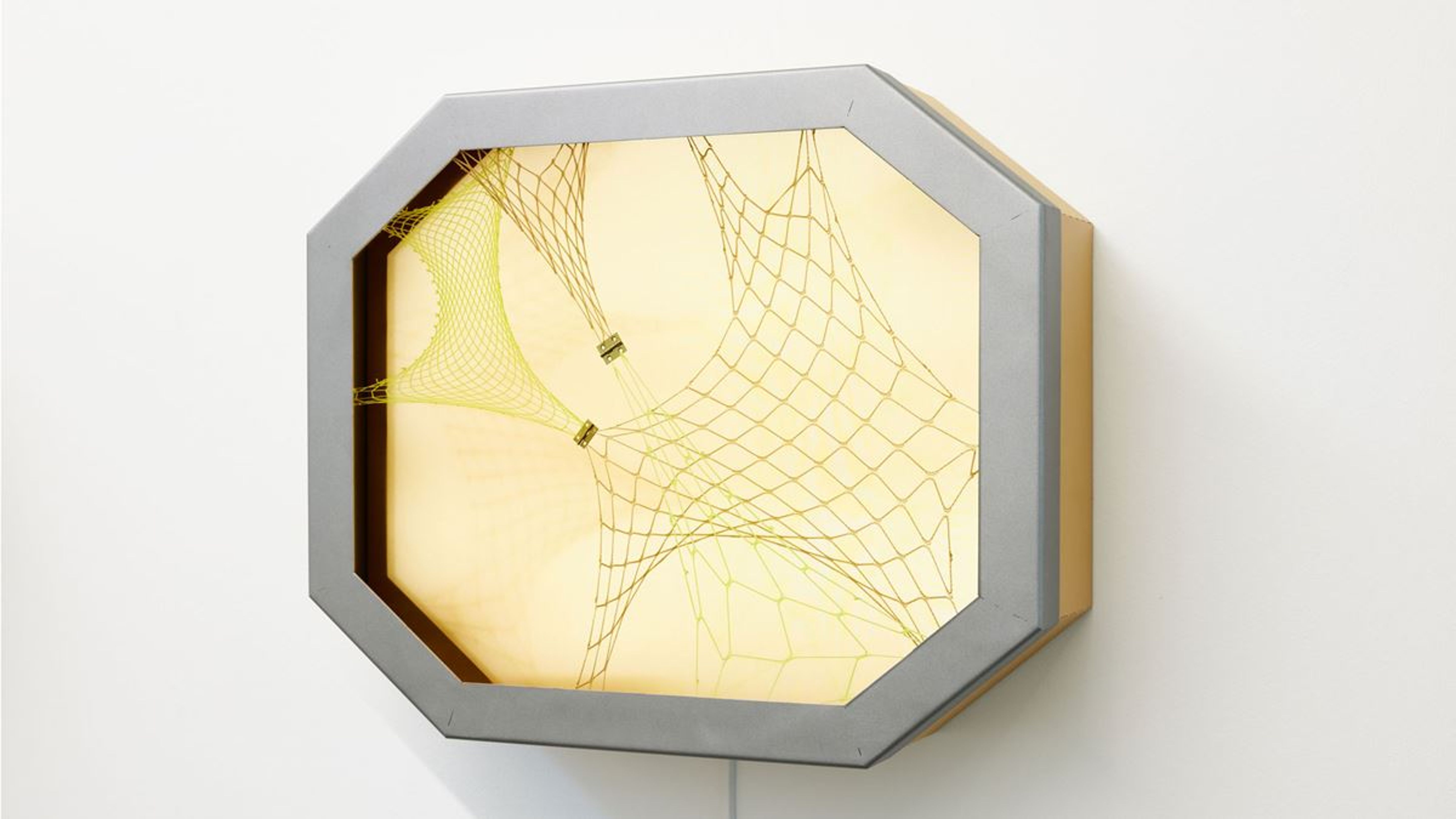 Un oggetto da parete ottagonale con design della rete giallo è appeso a una parete bianca.