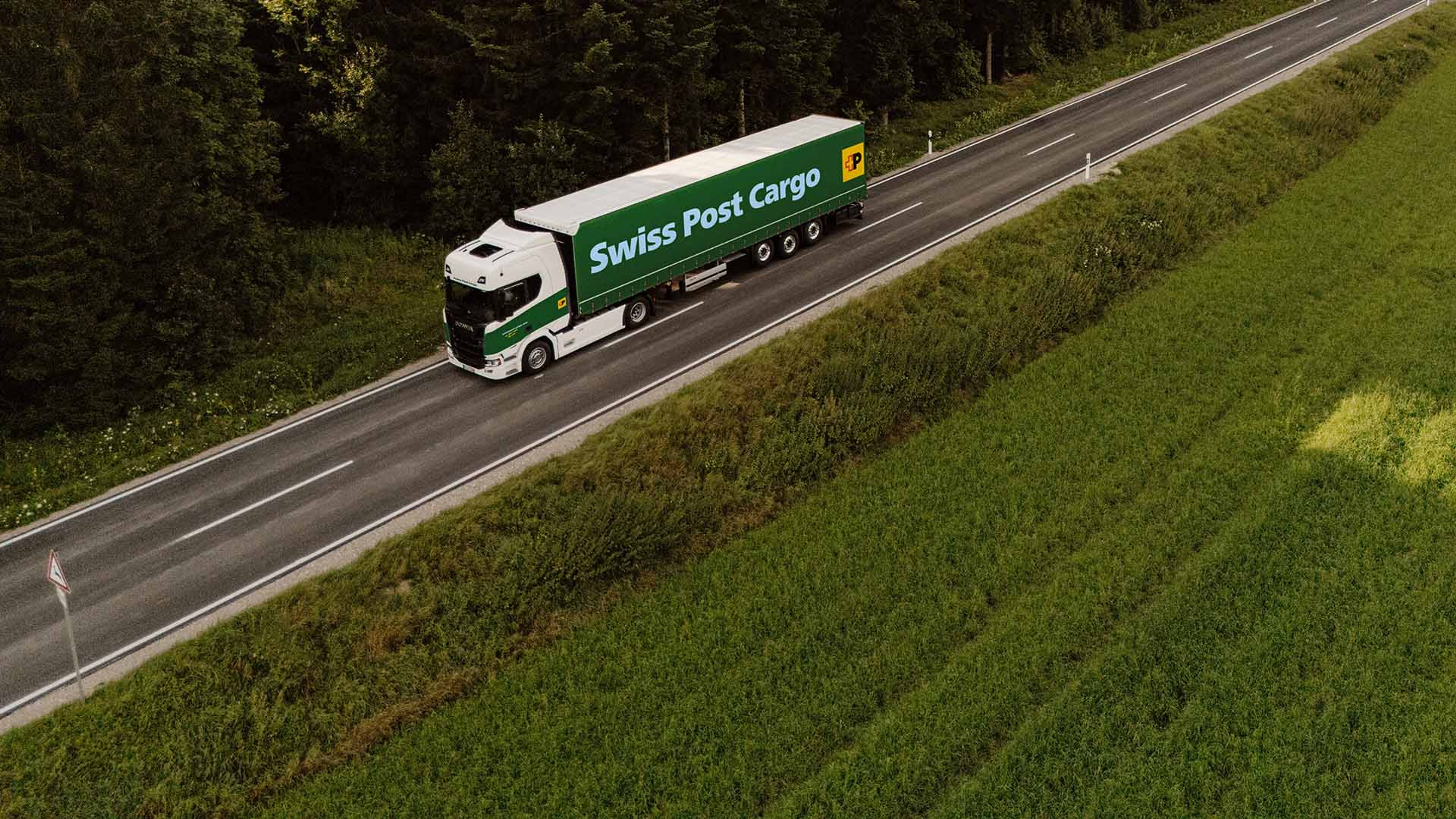 Un autocarro Swiss Post Cargo percorre una strada di campagna ai margini del bosco