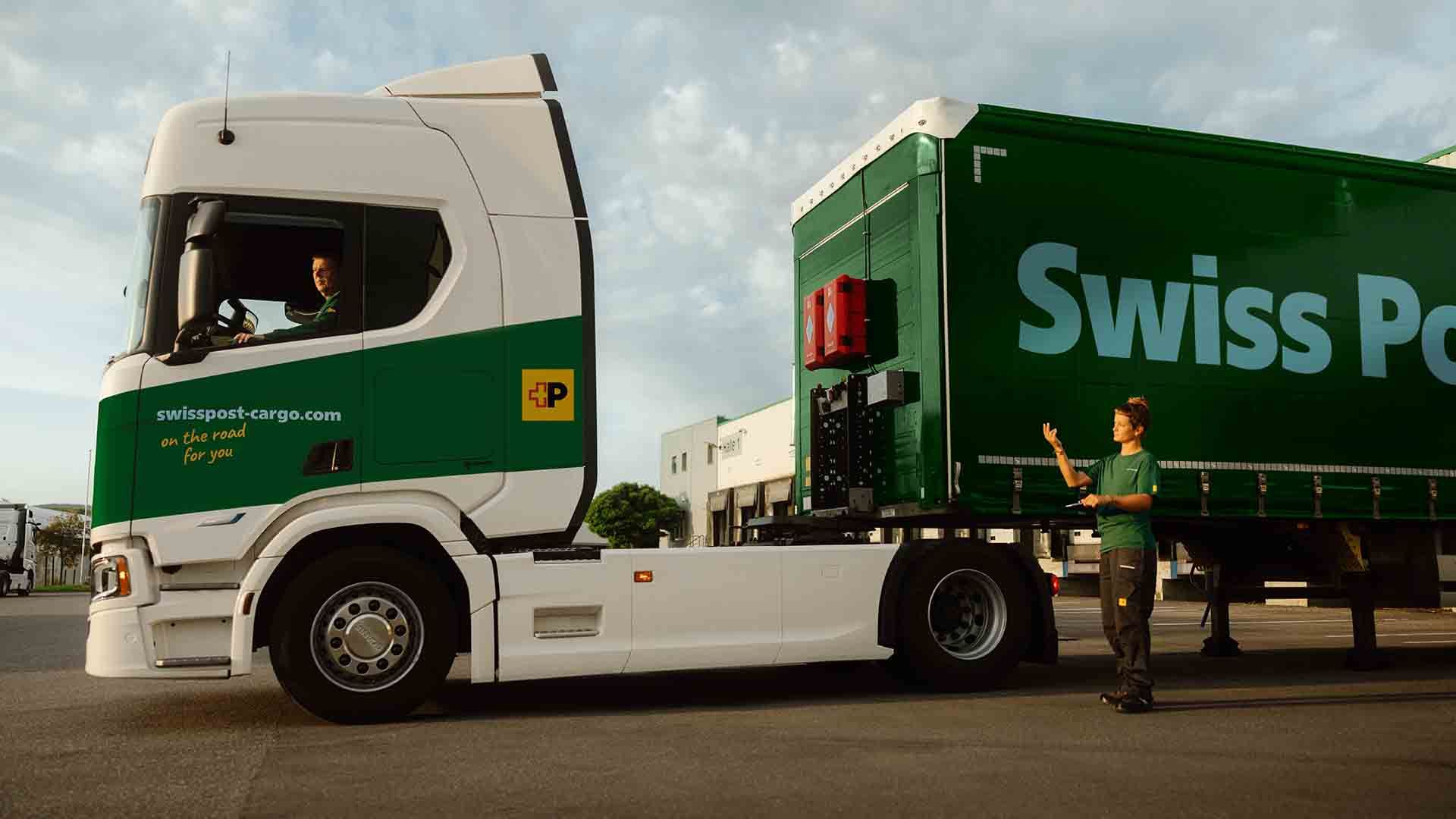 Un chauffeur de camion Swiss Post Cargo attelle une remorque, assisté par une collègue.