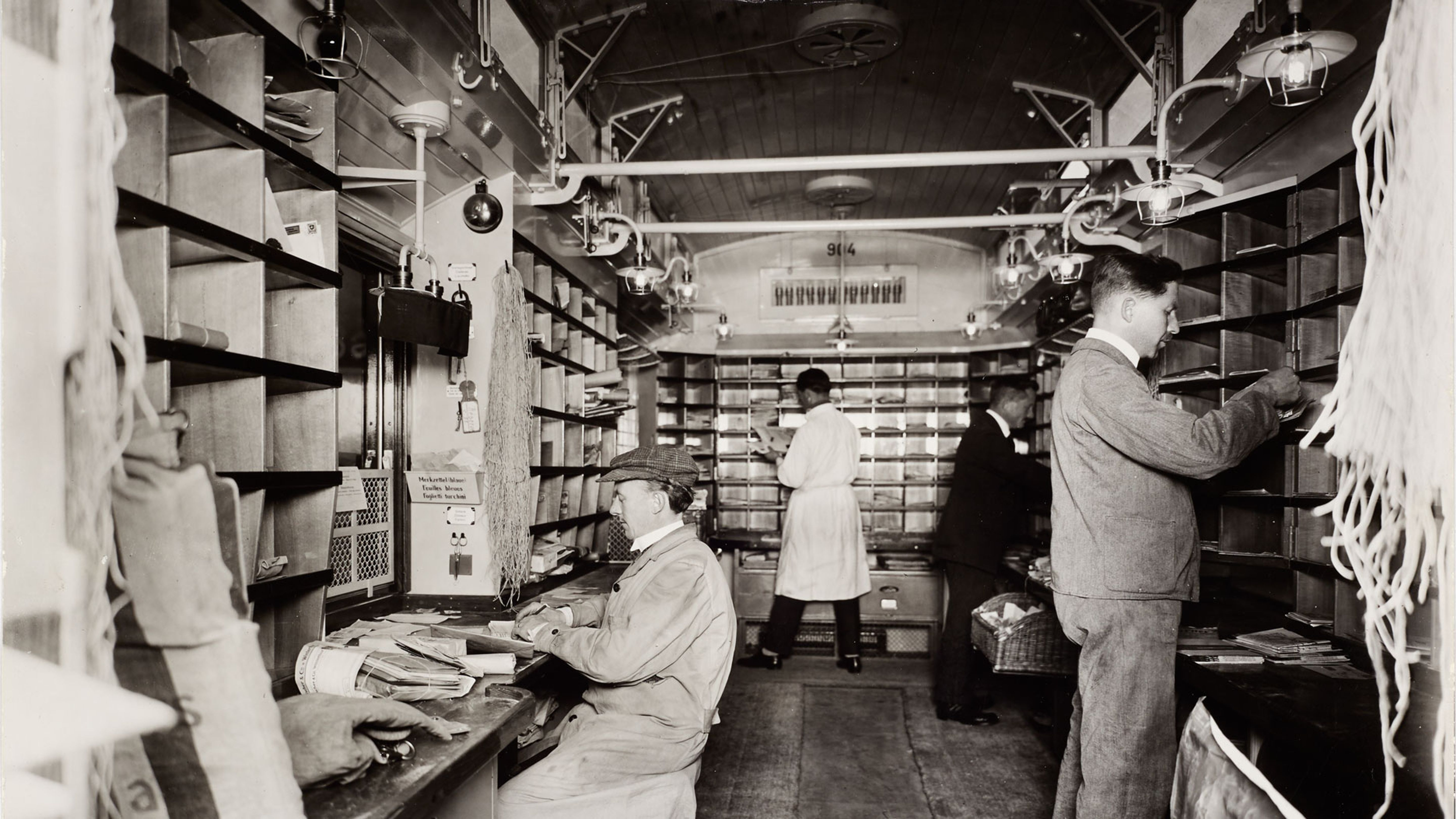Bahnpöstler bei der Unterwegssortierung im Büroraum des Bahnpostwagens auf der Strecke Basel–Belfort 1926. Quelle: Museum für Kommunikation