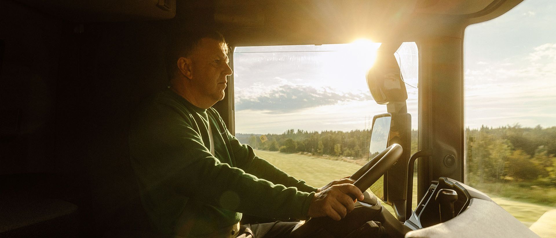 A Swiss Post Cargo truck driver steers his vehicle on a direct route through a sunny landscape.